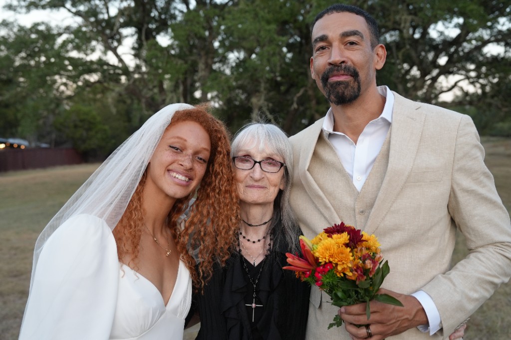 Juliana, Nancy, and Micah Salaberrios smiling together outdoors, holding a bouquet of autumn flowers